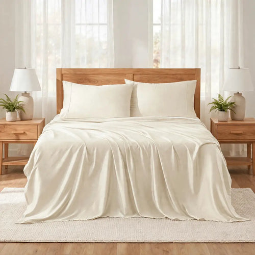 Las Mareas, A neatly made bed with a cream-colored sheet set, including a duvet cover and two pillows, styled in a bright, modern bedroom with a wooden headboard, bedside tables, lamps, and plants.