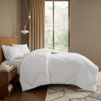 White comforter on a bed in a bedroom with a window and side table. king size