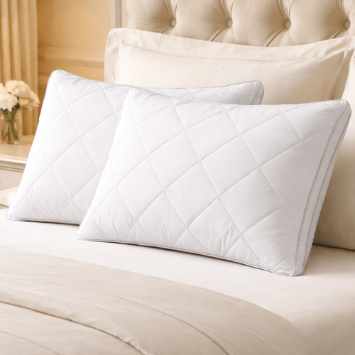 Two white quilted pillows on a bed with beige bedding and headboard.