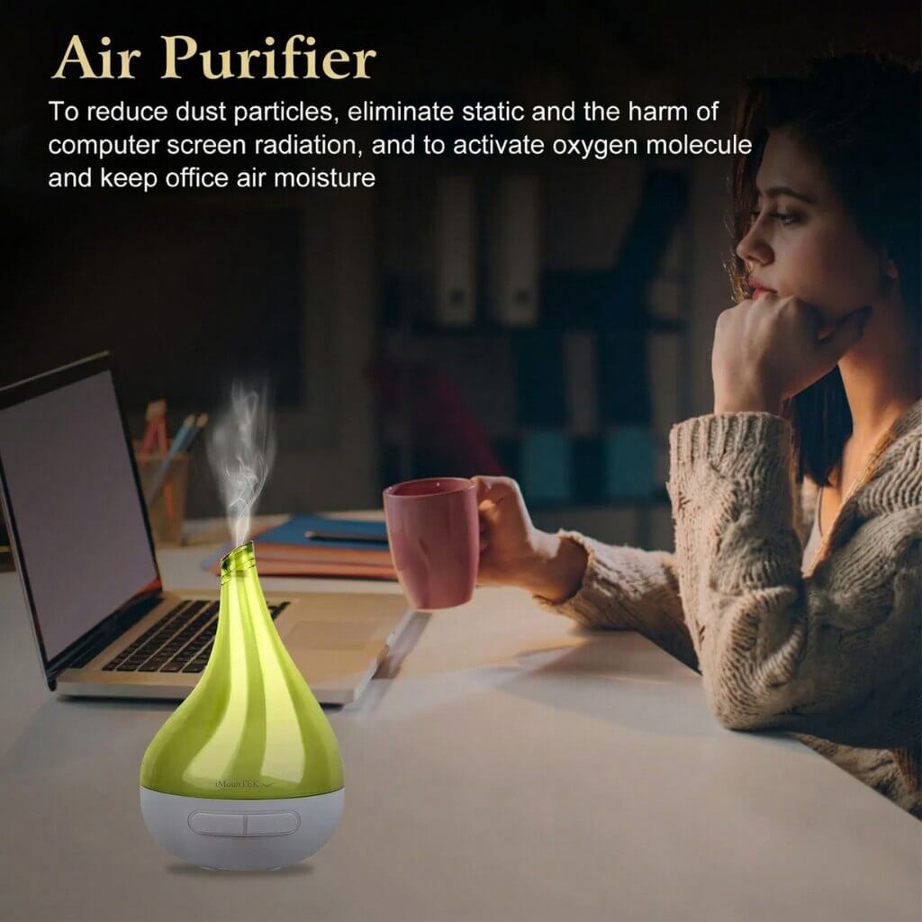 Woman sitting at a desk with a green air purifier, laptop, and pink mug.